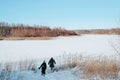 Back view of couple of travelers walking in snowdrift on frozen lake near snowy forest sunny winter day. Royalty Free Stock Photo