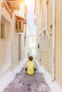 Back view of cute boy sitting on the steps on street in old greece town, Crete island, Greece. Summer landscape