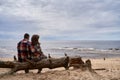 Back view of a cute couple with matching shirts sitting on a tree trunk on a sandy beach Royalty Free Stock Photo