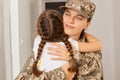 Back view of cute dark haired kid with mother, soldier woman wearing camouflage uniform and cap posing with her daughter, child Royalty Free Stock Photo