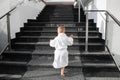 Back view of cute funny caucasian blond kid boy wearing white pool spa bathrobe walking upstairs on big marble staircase Royalty Free Stock Photo