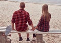 Back view of a cute hipster couple, sits on a bench in the middle of the beach and watch a sea. Royalty Free Stock Photo