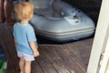 Back view of cute little caucasian toddler boy stand alone in ship garage wooden floor dock and looking on inflatable