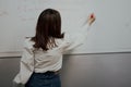 Back view of a cute young englisg language teacher in white blouse writing on a board and giving a class Royalty Free Stock Photo