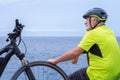 Back view of cyclist man resting at sea on the cliff after activity with his electro bike. Looking away at horizon
