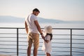 Back view of daughter with her father stand on heigh balcony in front of sea sunset. Dad with his little girl looking on