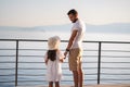 Back view of daughter with her father stand on heigh balcony in front of sea sunset. Dad with his little girl looking on
