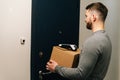 Back view of delivery man standing front door of customer apartment with cardboard box and contactless payment POS Royalty Free Stock Photo