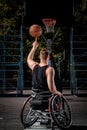 Back view of a disabled basketball player in wheelchair spinning basketball on his finger on open gaming ground.