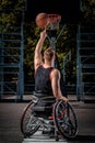 Back view of a disabled basketball player in wheelchair spinning basketball on his finger on open gaming ground.