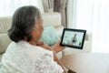 Back view of elderly woman making video call with her doctor with her feeling sore throat on digital tablet online healthcare