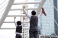 Back view of excited Asian businessman and son keeping arms raised standing outdoors with city in background. Family business man Royalty Free Stock Photo