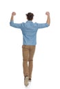 Back view of excited guy in denim shirt holding arms in the air