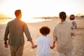 Back view of family walking on the beach with two kids, holding hands, enjoying sunset on seaside Royalty Free Stock Photo