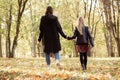 Back view of family of young woman mother and teenage girl walking among trees in forest park in autumn, holding hands. Royalty Free Stock Photo