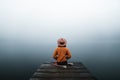 Back view of fashioned young woman sitting on wooden dock looking at view on a misty morning. Royalty Free Stock Photo