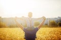 Back view of a father with his son on the shoulders standing in a field and city on summer sunset