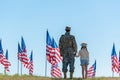 View of father in military uniform holding hands with child near american flags