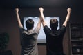 Back view of father and son watching tv at night in the living room, Two young men in full rear view enjoying tv entertainment, AI