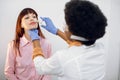 Back view of female afro doctor ent, doing nose examination of her patient. Young Caucasian lady, sitting on the chair