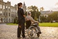 Back view of female care taker in protective mask spending time with senior handicapped man in wheelchair wearing Royalty Free Stock Photo