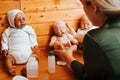 Back view of female doll maker holding caucasian rebeorn while sitting at table in homemade workshop.