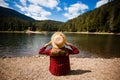 Back view of female tourist in hat with hands up enjoying freedom and amazing scenery of mountain lake. Royalty Free Stock Photo