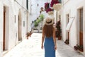 Back view of female tourist walking in old town. Travel woman in straw hat and blue dress enjoying vacation in Europe. Tourism and Royalty Free Stock Photo