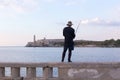 Back view of fisherman standing on the Malecon seawall stone railing, with the Morro Castle in the background