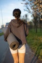 Back view fit woman holding yoga workout mat, sportswear, walking at city park after workout. Royalty Free Stock Photo