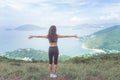 Back view of fitness woman standing on green mountain with her arms outstretched looking at sea landscape expressing