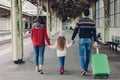 Back view of friendly family hold hands, carry suitcase, going to have voyage trip, pose on railway station platform. Young mother Royalty Free Stock Photo