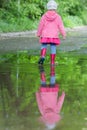 Back view full length portrait of little girl wearing red gumboots walking in big spring puddle Royalty Free Stock Photo