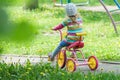 Back view full length portrait of preschooler girl riding kids pink and yellow tricycle on playground track Royalty Free Stock Photo