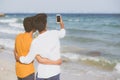 Back view gay portrait young couple smiling taking a selfie photo together with smart mobile phone at beach Royalty Free Stock Photo