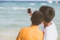 Back view gay portrait young couple smiling taking a selfie photo together with smart mobile phone at beach Royalty Free Stock Photo