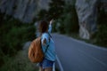 Back view girl with backpack stands on road with mountains on background at evening Royalty Free Stock Photo