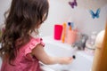 Back view. girl child washes hands with soap in the bathroom