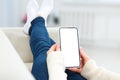 Back view of girl lying on sofa holding smartphone with white blank screen mockup. Lifestyle concept with digital technology Royalty Free Stock Photo