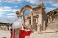 Back view of girl in red dress and white hat watches Temple of Hadrian ruins in antique Ephesus city, Turkey, on a sunny summer