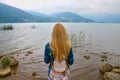 Back view of girl standing near water and looking at horizon with mountains Royalty Free Stock Photo