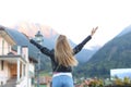 Back view of girl standing with raised hands in mountain village.