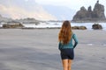 Back view of girl walking reflexive e tranquil on hidden amazing black beach on sunrise. Young female discovering wild paradisiac Royalty Free Stock Photo