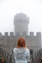 Back view girl wearing jeans jacket look distance on Fortification on top of the mountain, old castle. Mystical atmosphere, fog,