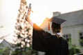 Happy graduated young woman in cap and gown talking with parent in mobile phone and looking certificated in hand so proud Royalty Free Stock Photo