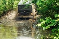 Back view of green russian off-road utility vehicle UAZ Hunter going up dirty road crossing river in forest among trees. Royalty Free Stock Photo