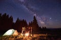 Group of tourists are standing around burning fire near the tents against backdrop pine forest under starry sky Royalty Free Stock Photo