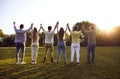 Back view of a group of friends standing in a row holding hands with their hands up outdoors. Royalty Free Stock Photo