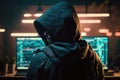 Back view of hacker in a hood with hidden face looks at the monitor screen with glowing code. Hacking and malware concept.