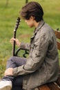 Back view of handsome teenage playing acoustic guitar with capo. Boy sitting on bench and playing music